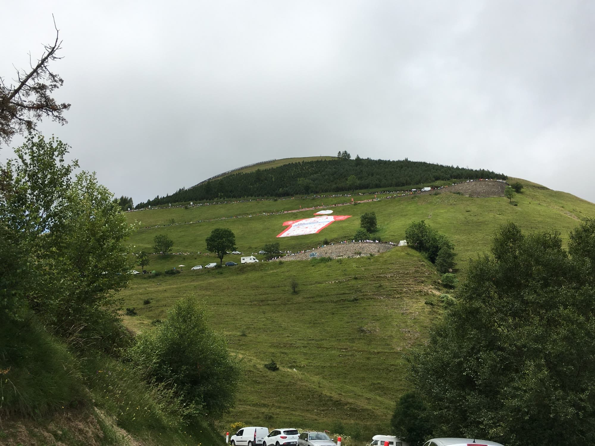 A green Pyrenean hillside at Peyragudes, with a giant cycling jersey laid out on the slope above the parked cars.