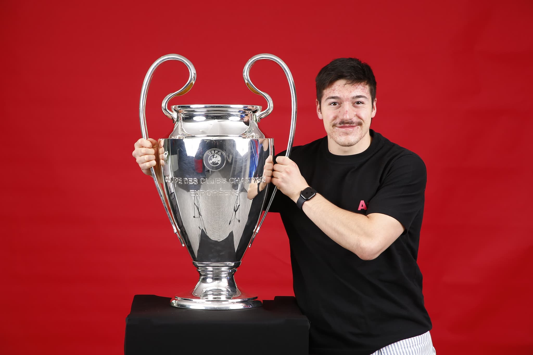 Standing beside the UEFA Champions League trophy against a red backdrop.