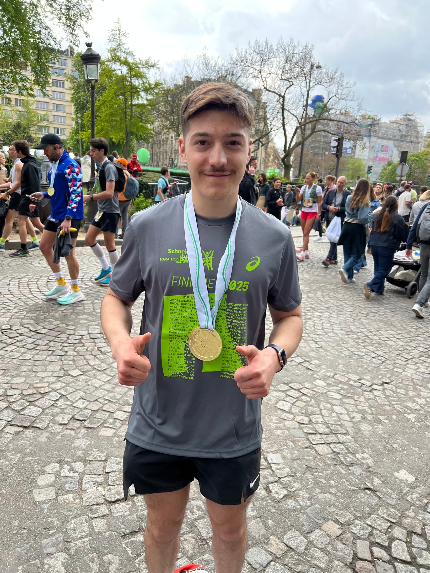Holding the finisher medal in the street after the Paris Marathon, runners still coming in behind.