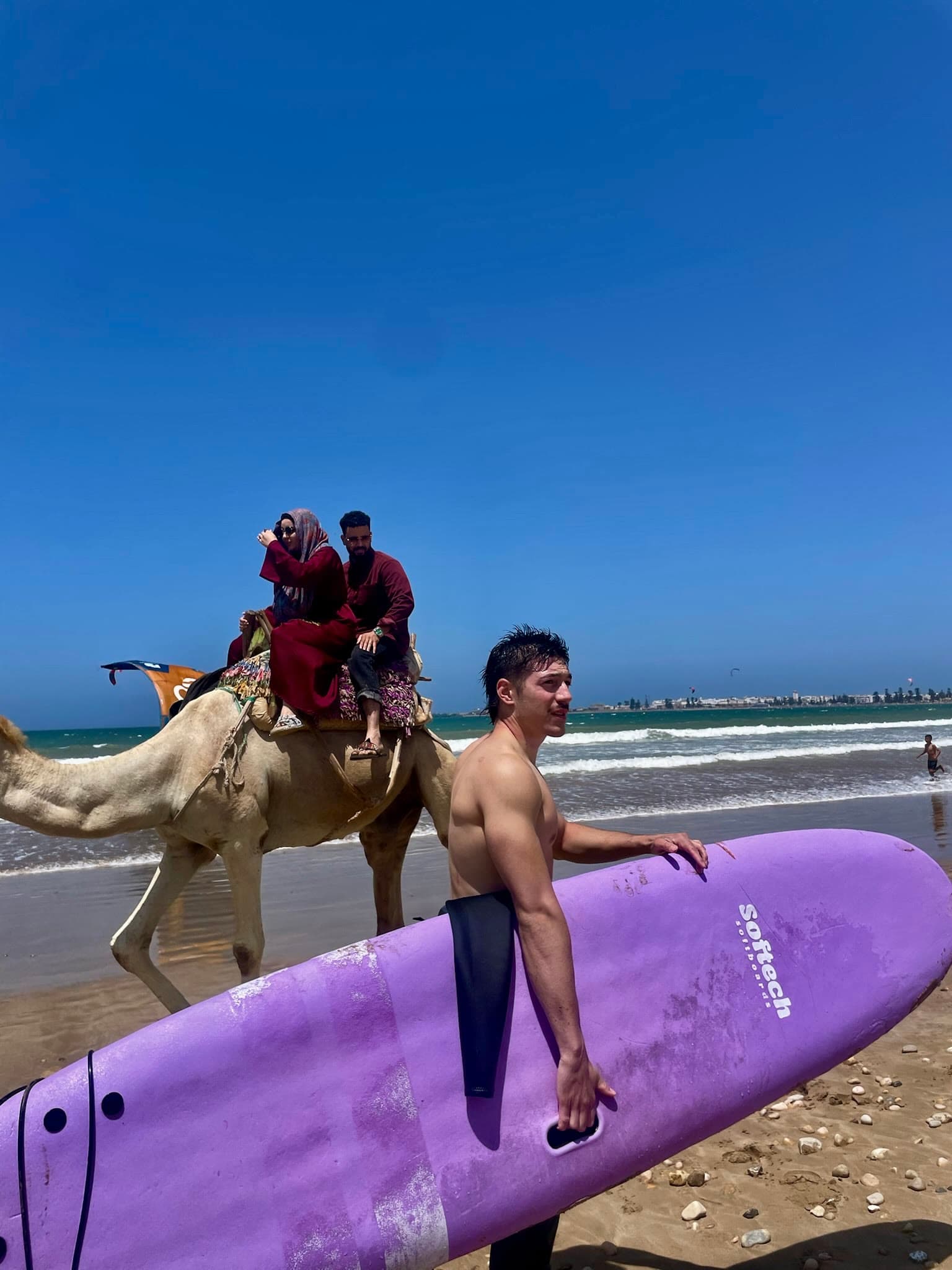 Walking back up the beach with a surfboard under one arm, the sea behind.